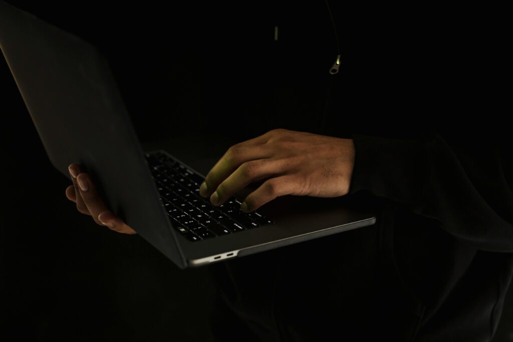 Silhouette of a person using a laptop in a dark environment, emphasizing online work or security.